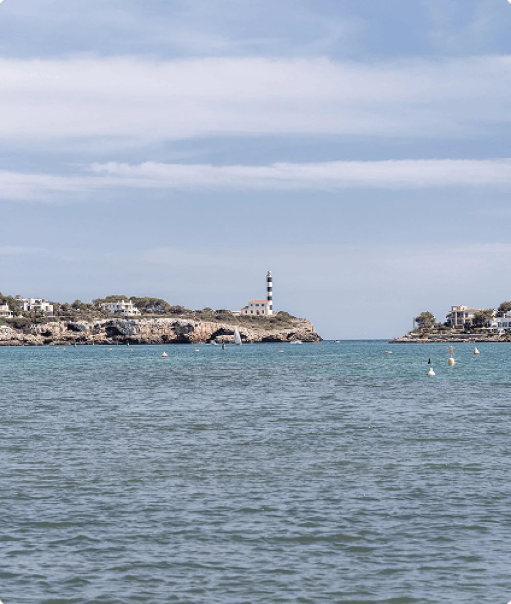 Vista del emblemático faro rayado y las tranquilas aguas del puerto de Porto Colom.